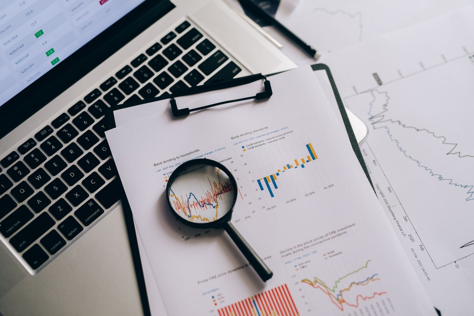 Magnifying glass over printed charts beside a laptop, comparing cruise quotes side by side